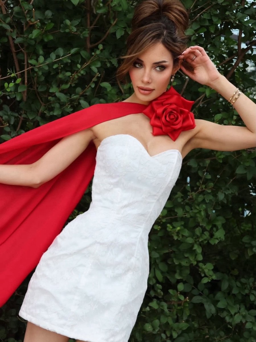 Nathalie in a white dress with a red rose cape